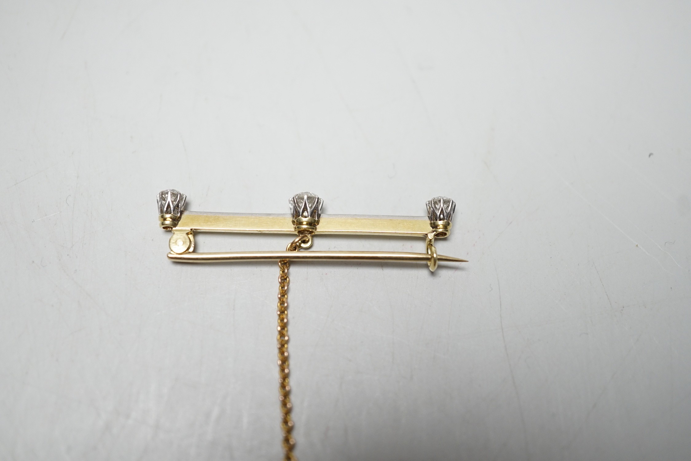 A yellow metal and three stone diamond set bar brooch, 36mm, gross weight 2.8 grams.